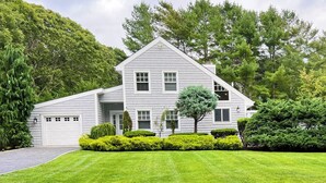 A two-story house with a garage, surrounded by well-maintained lawns and trees. - Pristine Remsenburg Retreat to Play & Work All Summer Long (Remsenburg)