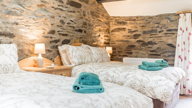 A cozy bedroom with stone walls, two beds with patterned bedding, bedside lamps, and a neatly made bed with a towel. - Middlefield Cottage, rural location close to lake (Coniston)