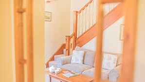 A cozy living room with a wooden staircase, a sofa, a coffee table, and a framed picture on the wall. - Middlefield Cottage, rural location close to lake (Coniston)