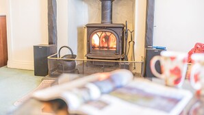 A cozy room with a wood-burning stove, a bookshelf, and a coffee table with a magazine. - Middlefield Cottage, rural location close to lake (Coniston)