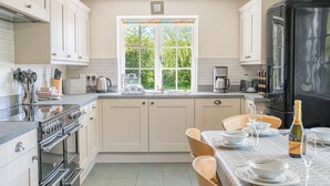 A modern kitchen with a dining area, featuring a large window, stainless steel appliances, and a black refrigerator. - Middlefield Cottage, rural location close to lake (Coniston)