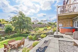 Ein Garten mit Whirlpool, Holzterrasse und einem gepflasterten Weg.