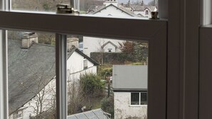 Blick durch ein Fenster auf ein Wohngebiet mit Häusern, einem Gewässer und Hügeln in der Ferne.