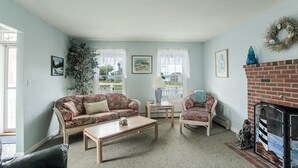 Un salon comprenant un canapé, un fauteuil, une table basse, une cheminée et une vue sur l’extérieur.