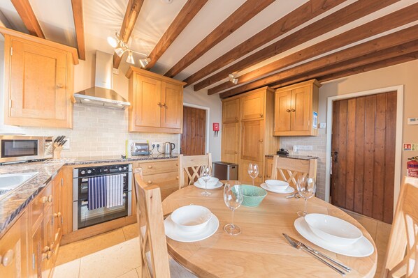 A kitchen with wooden cabinets, a built-in oven, a microwave, and a dining table set for four with white plates and glasses. - Stunning, unique tower with 2 bedrooms and incredible views (Nr. Hawkshead)