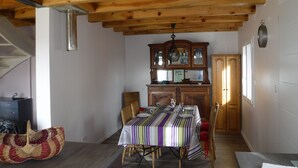 A dining area with a wooden ceiling, a striped tablecloth-covered table, wicker chairs, and a wooden cabinet with glass doors.