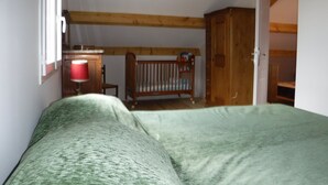 A bedroom with a wooden ceiling, a crib, a bedside table with a lamp, and a wardrobe.