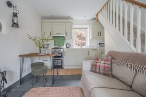 A compact kitchen with white cabinets, a dining area with a table and chairs, a sofa with a plaid throw, and a staircase with white railings. - Mountain cottage in stunning location with outstanding views (Coniston)