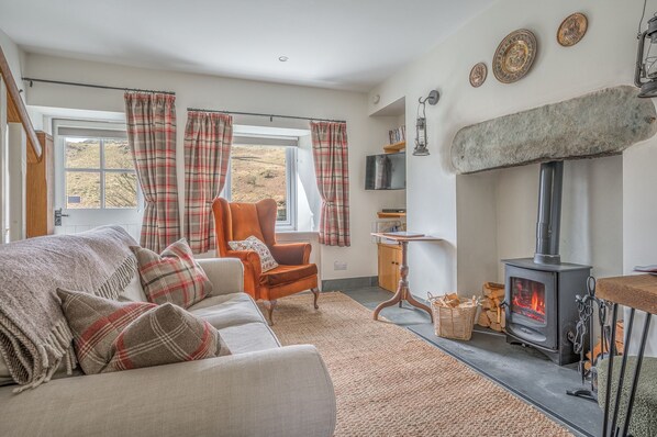 A cozy living room with a sofa, armchair, and a fireplace. - Mountain cottage in stunning location with outstanding views (Coniston)
