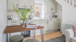 Une cuisine avec des meubles blancs, une table en bois et une vue sur l’extérieur.