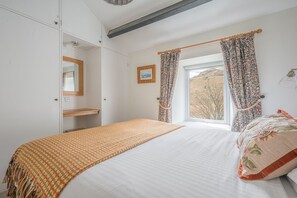A bedroom with a bed, a window with curtains, a bedside table, and a wardrobe. - Mountain cottage in stunning location with outstanding views (Coniston)