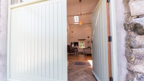 A room with a large sliding door, a wooden floor, a sofa, a chair, a TV, and a window with a view of greenery. - Mill Pool Barn, stunning riverside barn conversation in idyllic location (Coniston)