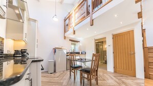 A modern kitchen with a dining area, wooden flooring, and a loft-style upper level. - Mill Pool Barn, stunning riverside barn conversation in idyllic location (Coniston)
