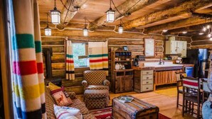 A cozy log cabin interior with a living room, sofa, armchair, and a small kitchen area. - Martin City Log Cabin, just a hop away from Glacier National Park (Martin City)
