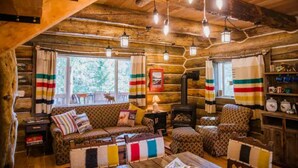 A cozy log cabin interior with a sofa, armchairs, a fireplace, and striped curtains. - Martin City Log Cabin, just a hop away from Glacier National Park (Martin City)