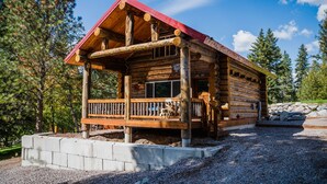 A log cabin with a red roof, a porch, and a stone wall foundation. - Martin City Log Cabin, just a hop away from Glacier National Park (Martin City)
