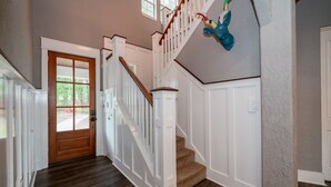 Una escalera con barandillas blancas y un pasamanos de madera, que lleva a un rellano con una puerta de madera.