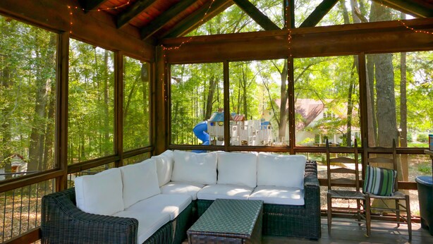Un área de estar al aire libre con techo de madera, ventanas amplias y vistas al bosque.
