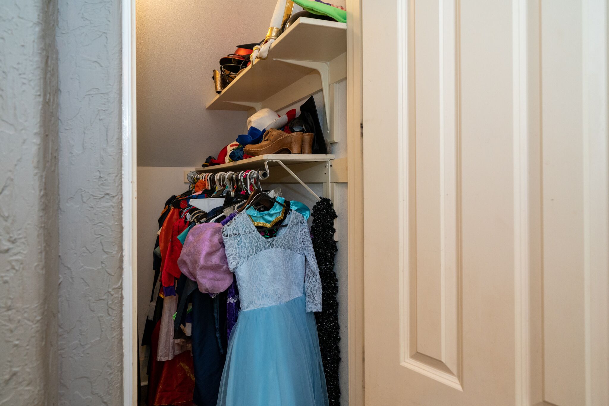 A closet with shelves and hanging space, containing various clothing items and shoes.