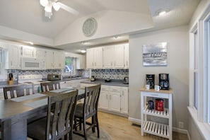 A kitchen with white cabinets, a microwave, a stove, and a dining area with a table and chairs. - AMAZING COVE! 3 Bed/2Ba Lakefront Home - Hot Tub, Smart TVs, EV Charger, Firepit (Eldon)