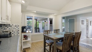 A kitchen with a dining area, white cabinets, a coffee maker, and a window with a view of greenery. - AMAZING COVE! 3 Bed/2Ba Lakefront Home - Hot Tub, Smart TVs, EV Charger, Firepit (Eldon)