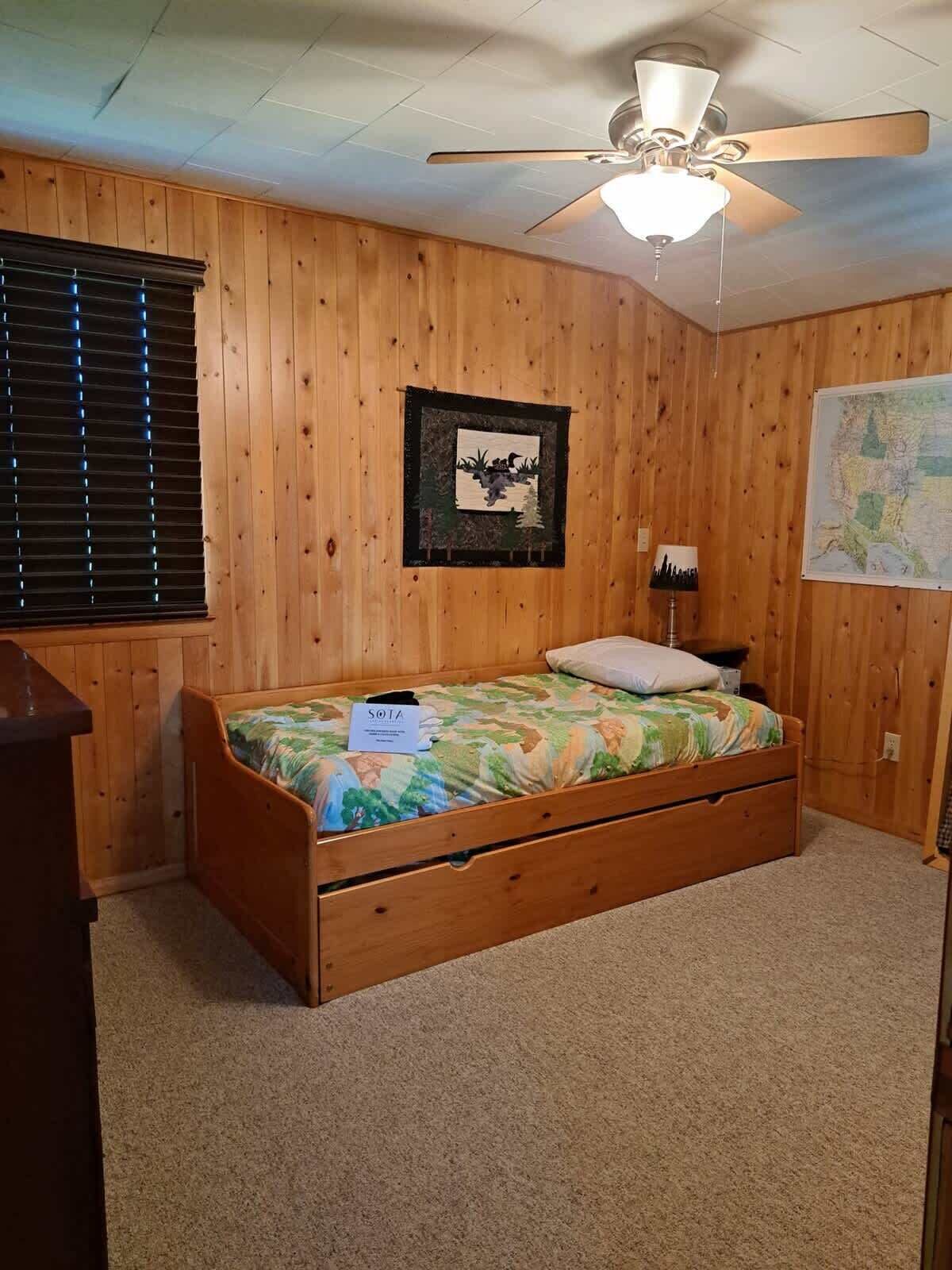 Un dormitorio con una cama litera de madera, un ventilador de techo, un mapa en la pared y un cuadro enmarcado.