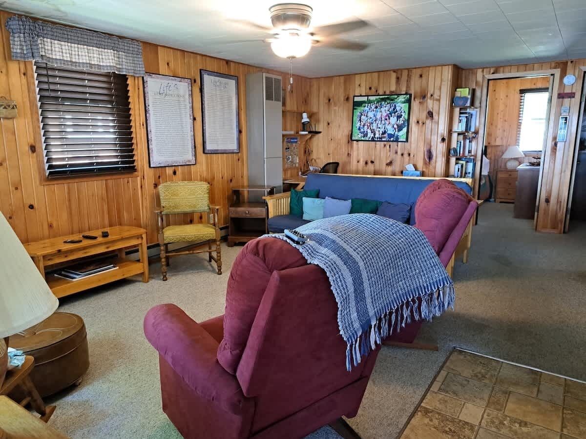 A room with a wooden interior, a blue sofa, a red armchair, a yellow armchair, a wooden cabinet, and a television on the wall.