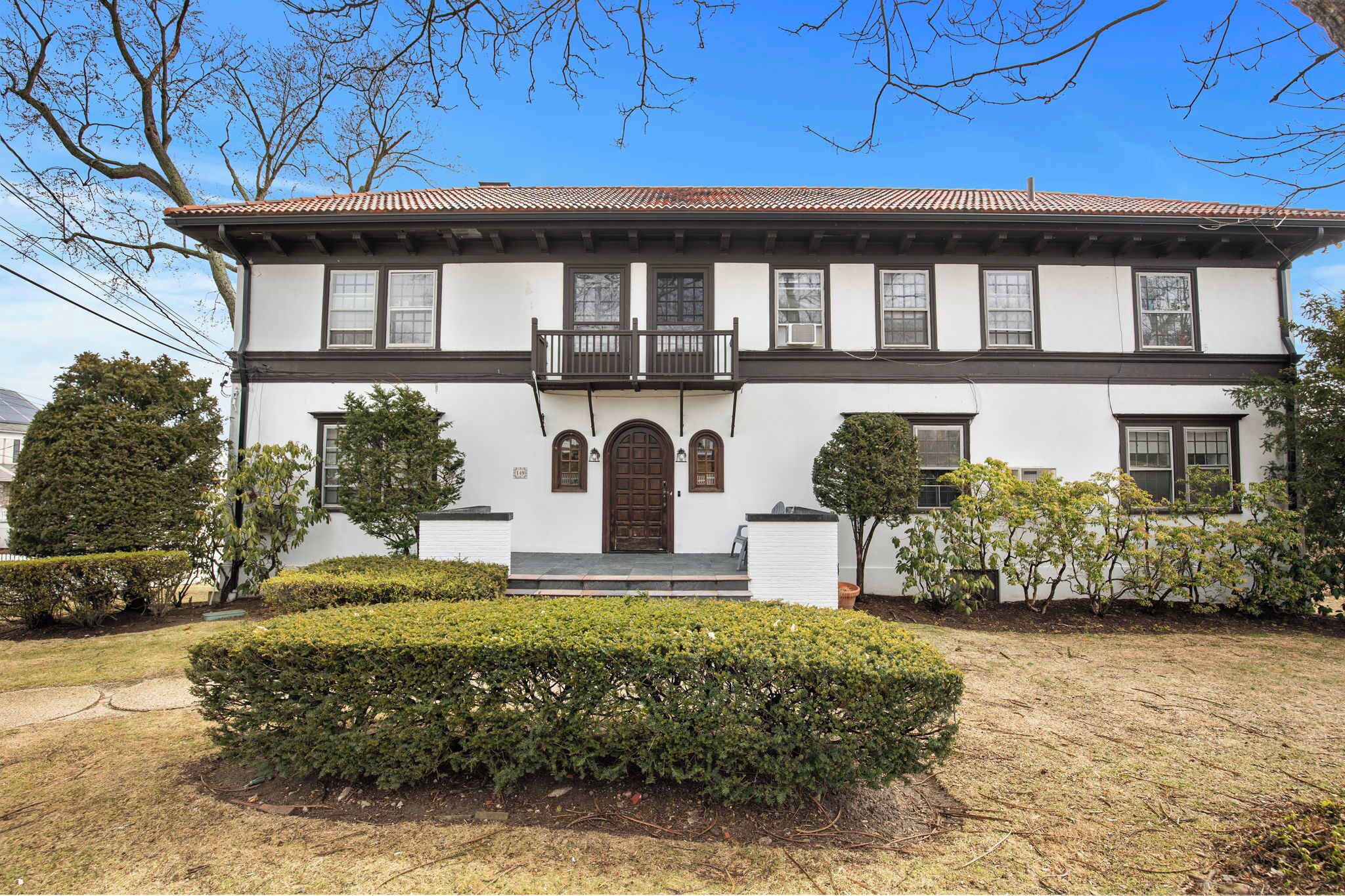 A two-story house with a central entrance, a balcony on the upper floor, and a well-maintained front yard with hedges.