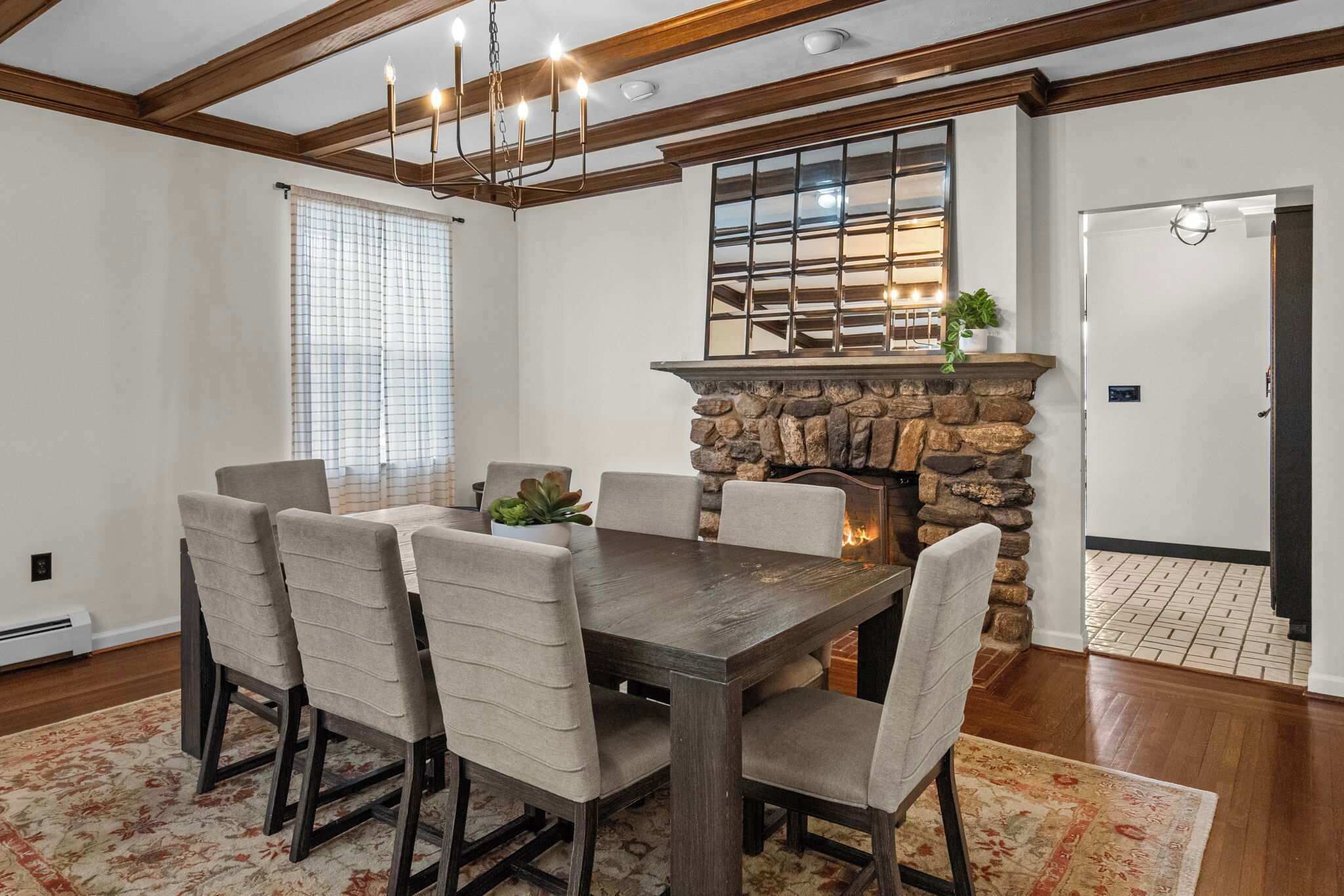 A dining area with a wooden table and chairs, a stone fireplace, and a large window with blinds.