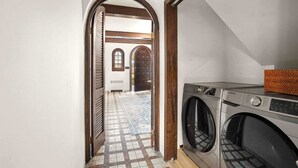 A laundry room with a washing machine and dryer, a patterned floor, and an arched doorway leading to a hallway with a tiled floor and a door. - Spacious 3b/3b Mediterranean in White Plains (White Plains)