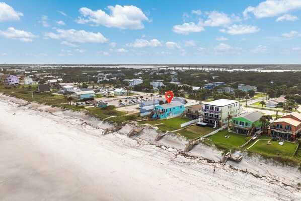 Uma área residencial costeira com casas, uma praia e uma ponte ao fundo.