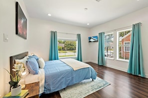 Un dormitorio con cama, televisor y ventanas amplias con cortinas.