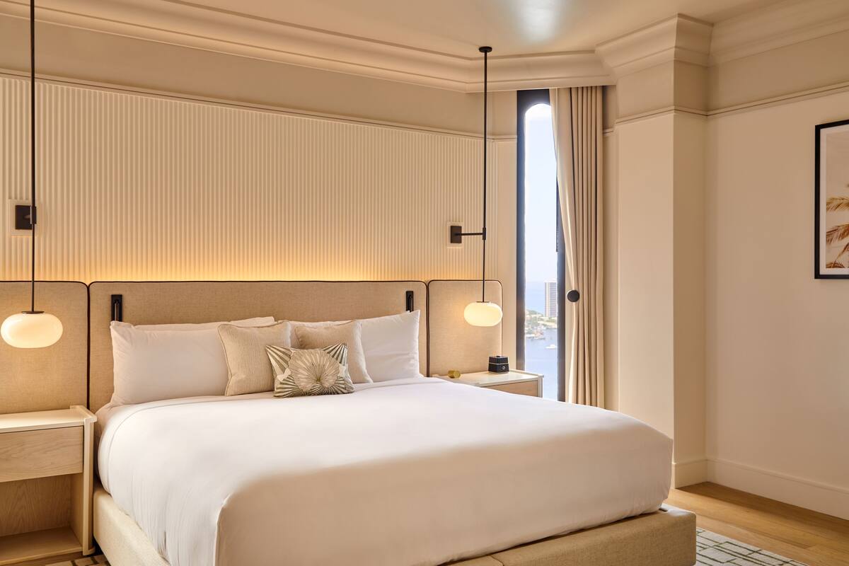 A neatly arranged hotel room with a large bed, bedside tables, a nightstand, and a window with curtains.