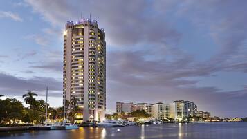 A high-rise hotel with multiple balconies, a marina with yachts, and a waterfront view.