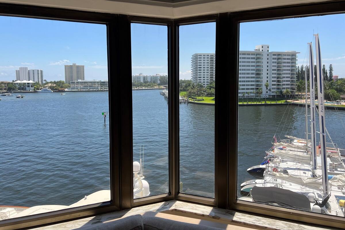 A view from a room with large windows overlooking a marina with boats and a cityscape in the background.