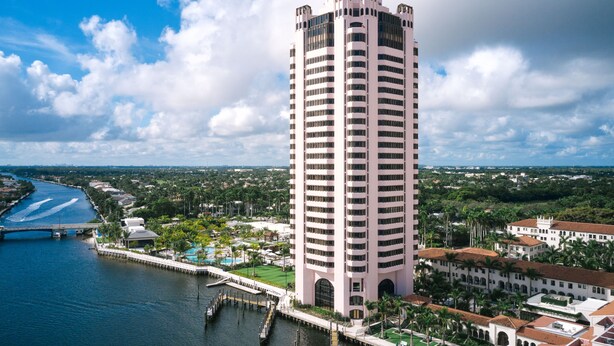 A tall hotel with a modern design, located near a waterfront with a dock and a bridge.