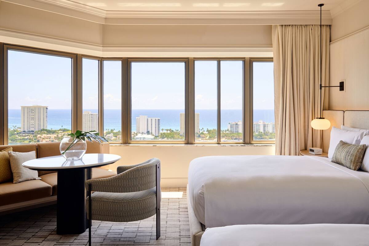 A hotel room with a large bed, a sofa, a small table, and a view of the ocean.