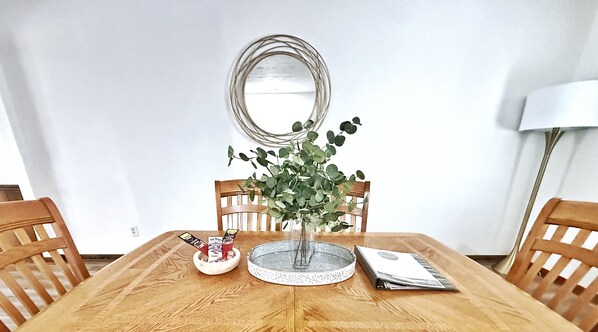 Una mesa de madera para comer con un florero de follaje verde, una bandeja decorativa y un menú.