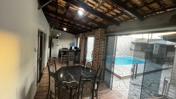 A spacious patio area with a dining table and chairs, a kitchen in the background, and a view of a swimming pool. - House with pool and barbecue. (Cuiaba)
