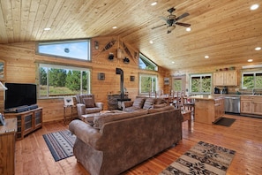 A spacious living room with a large brown sofa, a flat-screen TV, and a stone fireplace.