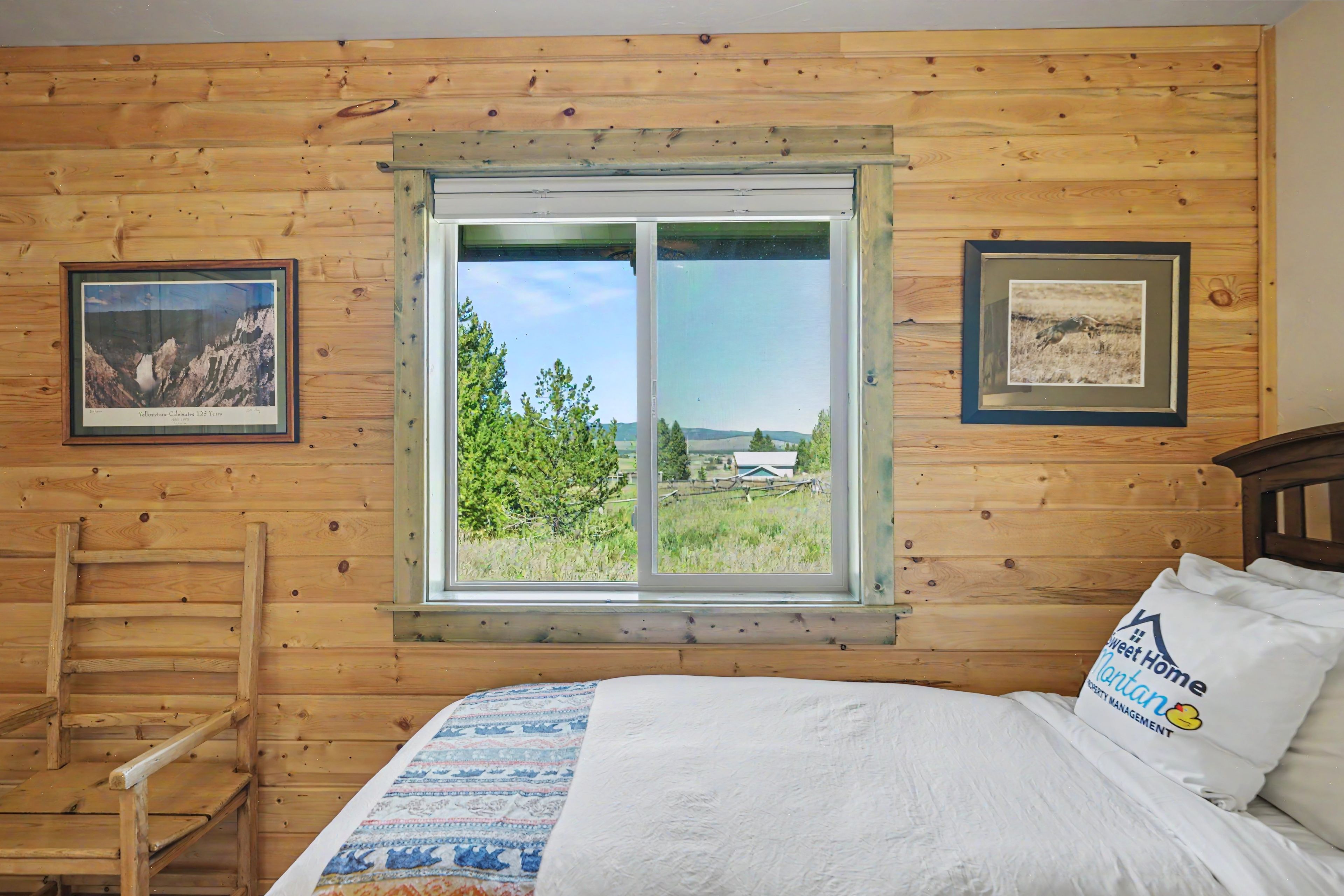 Una habitación de cabaña de madera con una cama, un ventanal con vistas a zonas verdes y dos cuadros en las paredes.