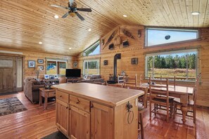 Un interior de cabaña espacioso con una gran mesa de madera para comer, una zona de estar acogedora y un televisor.