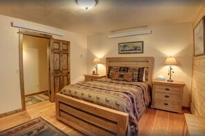 Un dormitorio con una cama de madera, dos mesitas de noche con lámparas, una puerta de madera y un cuadro enmarcado en la pared.