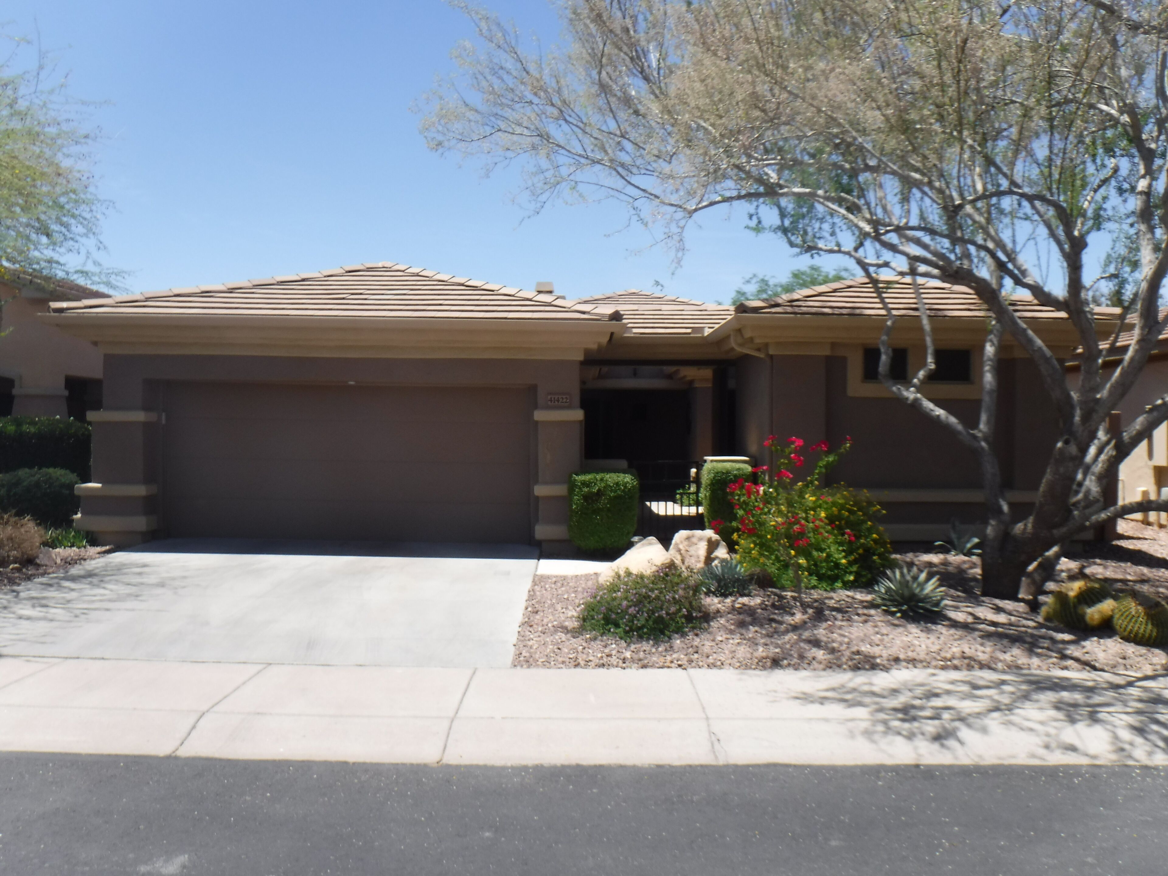 A residential house with a garage, a driveway, and a landscaped garden with various plants and flowers.