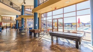 A spacious indoor area with a pool table, foosball table, and seating area, with large windows offering views of an outdoor pool and buildings. - NW Phoenix in Gated Anthem Country Club - House + Guest Casita (Phoenix (Anthem))