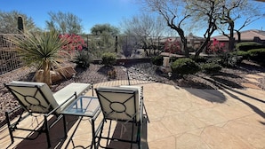 An outdoor patio with two chairs and a table, surrounded by a garden with various plants and a fence. - NW Phoenix in Gated Anthem Country Club - House + Guest Casita (Phoenix (Anthem))