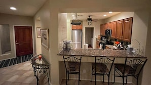 A kitchen with a granite countertop, four metal chairs, a refrigerator, and wooden cabinets. - NW Phoenix in Gated Anthem Country Club - House + Guest Casita (Phoenix (Anthem))