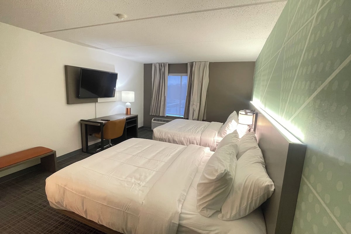 A hotel room with two beds, a desk, a chair, a television, and a window with curtains.