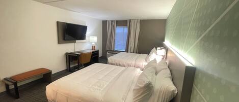 Hotellihuone, jossa on kaksi sänkyä, työpöytä, tuoli, televisio ja ikkuna, jossa on verhot.