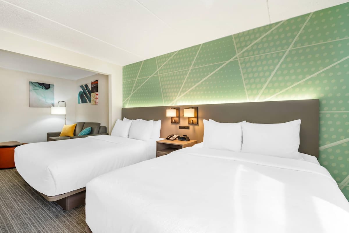 A hotel room with two beds, a nightstand with a phone, and a wall with abstract art.